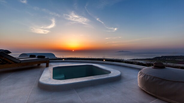 A rooftop terrace with a hot tub, lounge chairs, and a sunset view. - Villa Vinea (Santorini)
