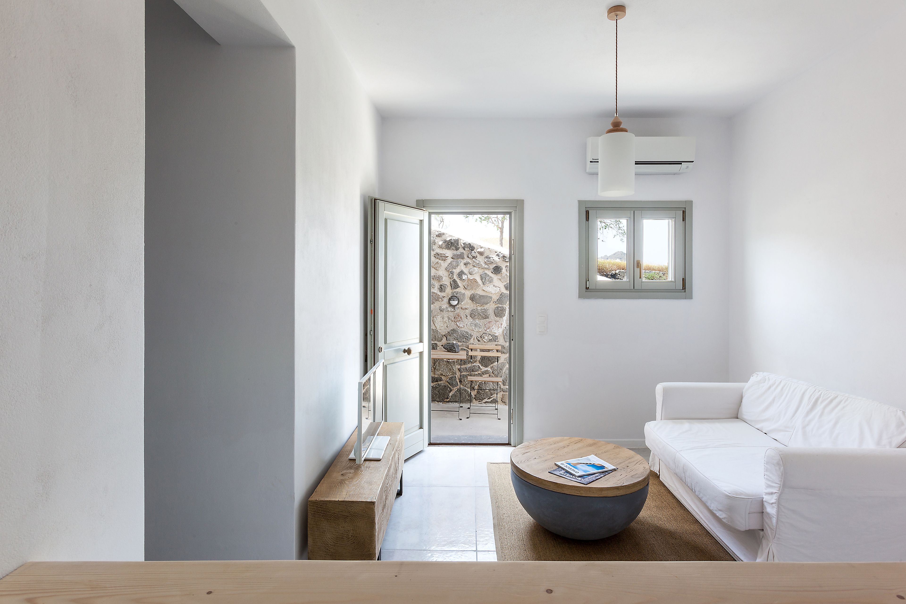 A modern, minimalist living room with a white sofa, a round coffee table, and a stone wall visible through an open door.