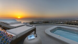 A rooftop pool area with lounge chairs and a hot tub, overlooking a cityscape at sunset. - Villa Vinea (Santorini)