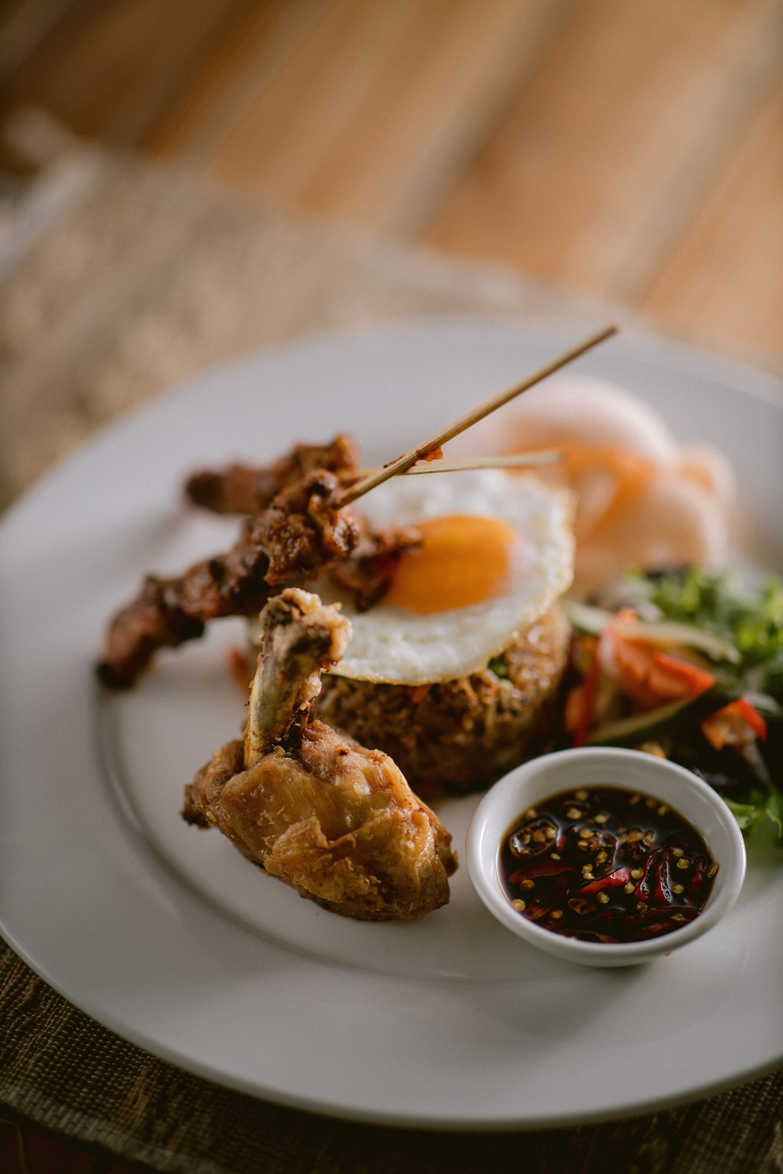 Un plato con brochetas de carne, un huevo frito y un recipiente pequeño con salsa.
