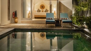 Een tweelaags gebouw met een balkon, zwembad en een zitgedeelte met stoelen en een parasol.