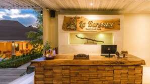 Een houten receptiebalie, een bord met de tekst 'La Belleuse', en een ontvangsthal met uitzicht op het omliggende landschap.