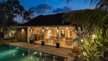 A poolside area with a dining area, a bicycle, and a well-lit interior.