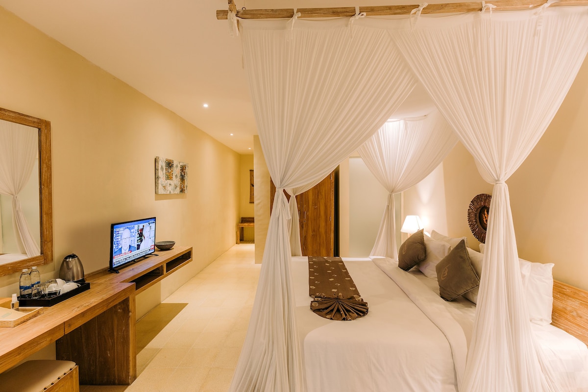 A bedroom with a four-poster bed, a wooden desk, a television, and a bedside table with a lamp.