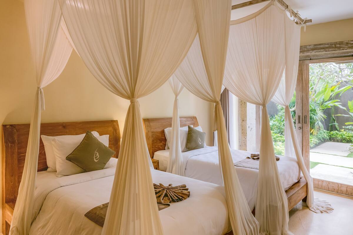Een slaapkamer met vier bedden, elk voorzien van witte lakens en groene kussens, en een hemelbed op de voorgrond.