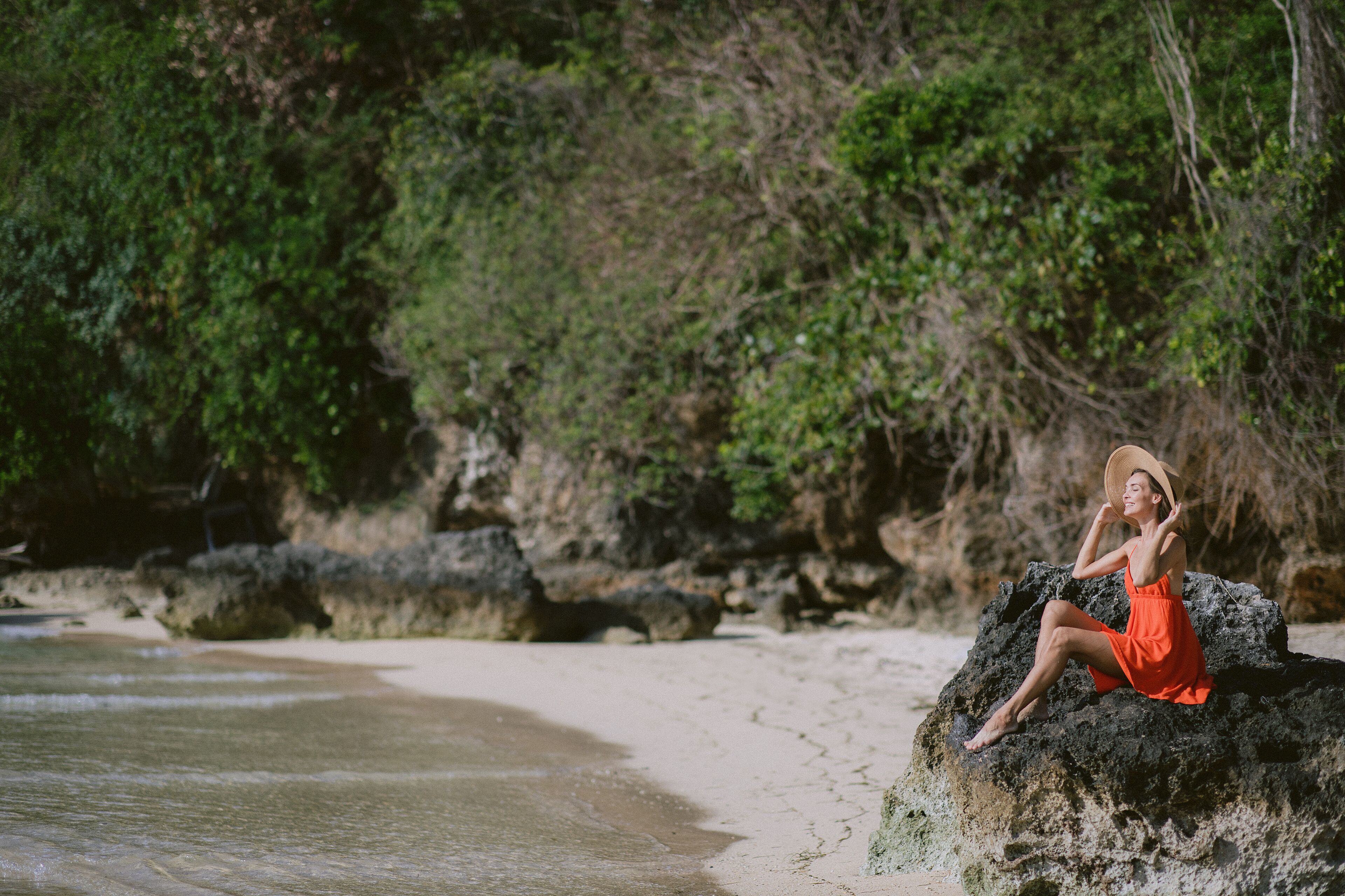 A person sitting on a rock by a beach with greenery in the background.