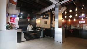 A hotel reception area with a modern design, including a reception desk labeled "RECEPTION," a staircase in the background, and a television screen displaying content. - Hotel Mandakini (Jakholi)