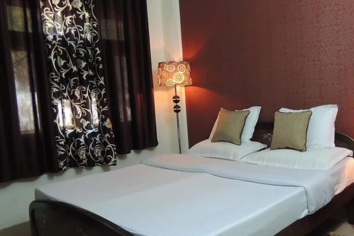 Una habitación de hotel con una cama, dos lámparas de noche, una mesita de noche y una cortina estampada con motivos florales.