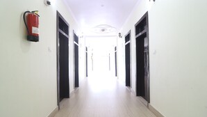 A long, well-lit hallway with doors on both sides, a fire extinguisher mounted on the wall, and a ceiling light fixture. - Hotel Mandakini (Jakholi)