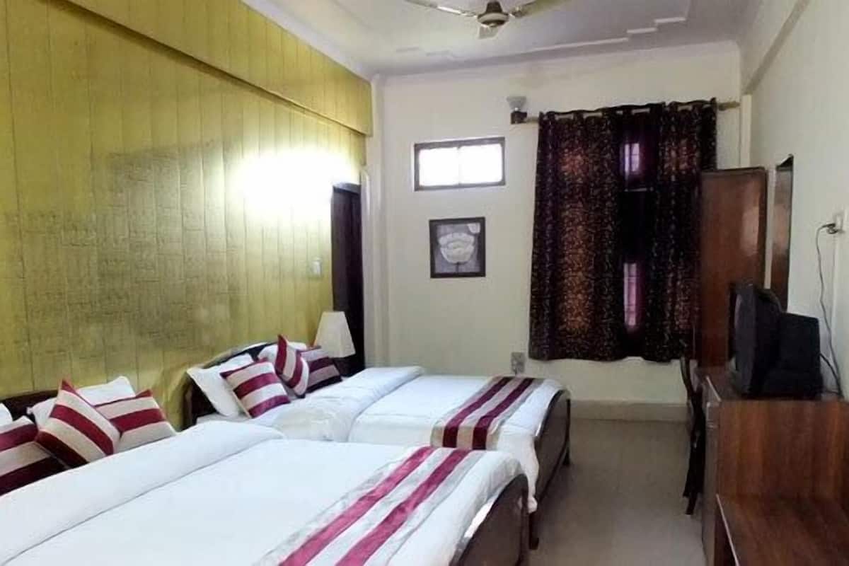 Una habitación de hotel con tres camas, televisión, ventana con cortinas y ventilador de techo.