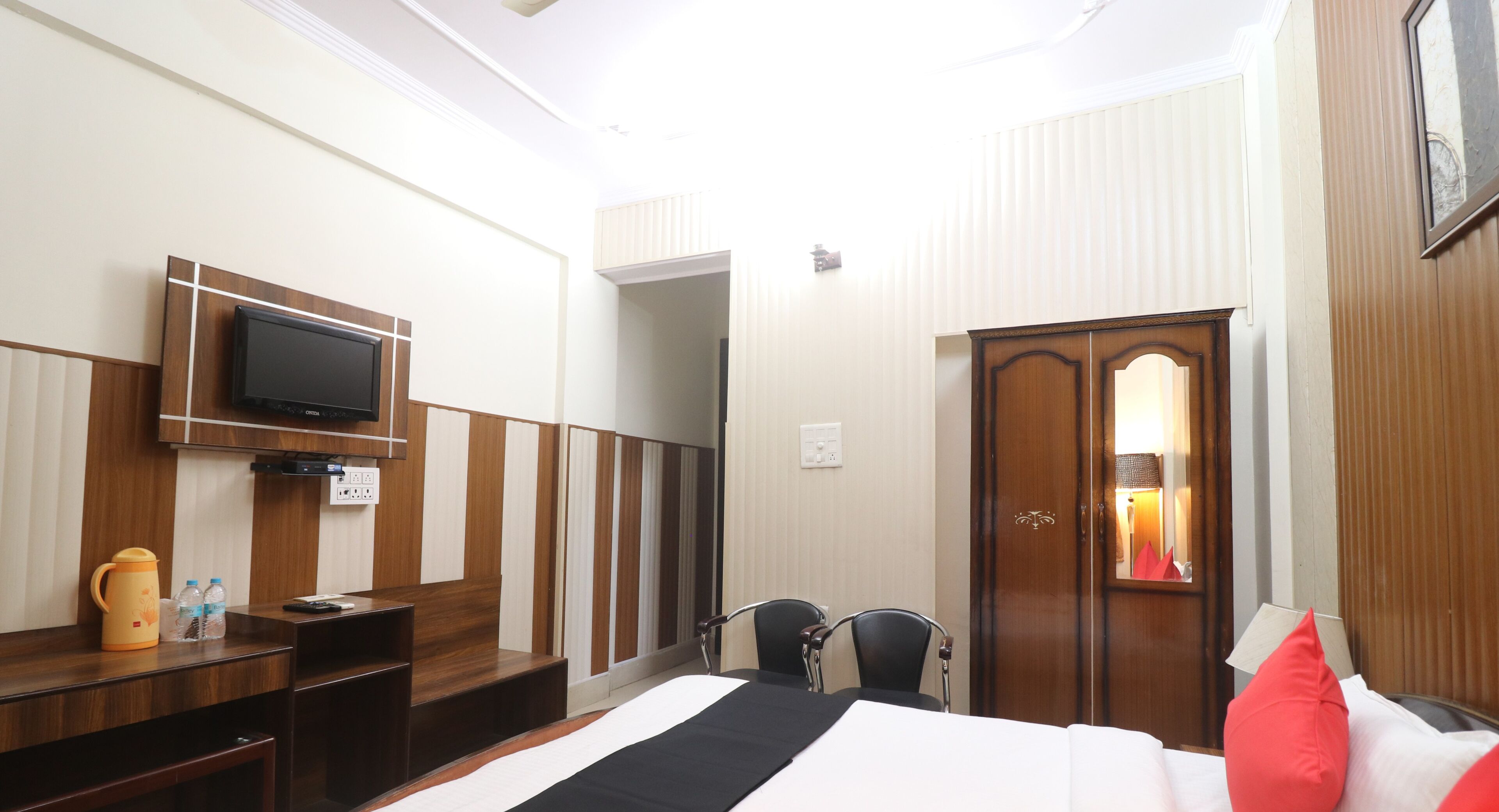 A hotel room with a bed, a desk with a television, a wardrobe, and a mirror.