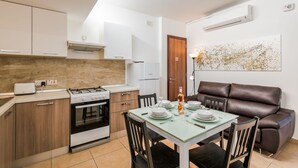Una cocina compacta con electrodomésticos modernos, un comedor con mesa de vidrio y un sofá de cuero marrón.