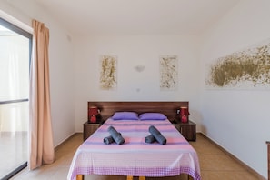 Ein Schlafzimmer mit einem Bett, zwei Nachttischen, einem Fenster mit Vorhängen und Wandbildern.