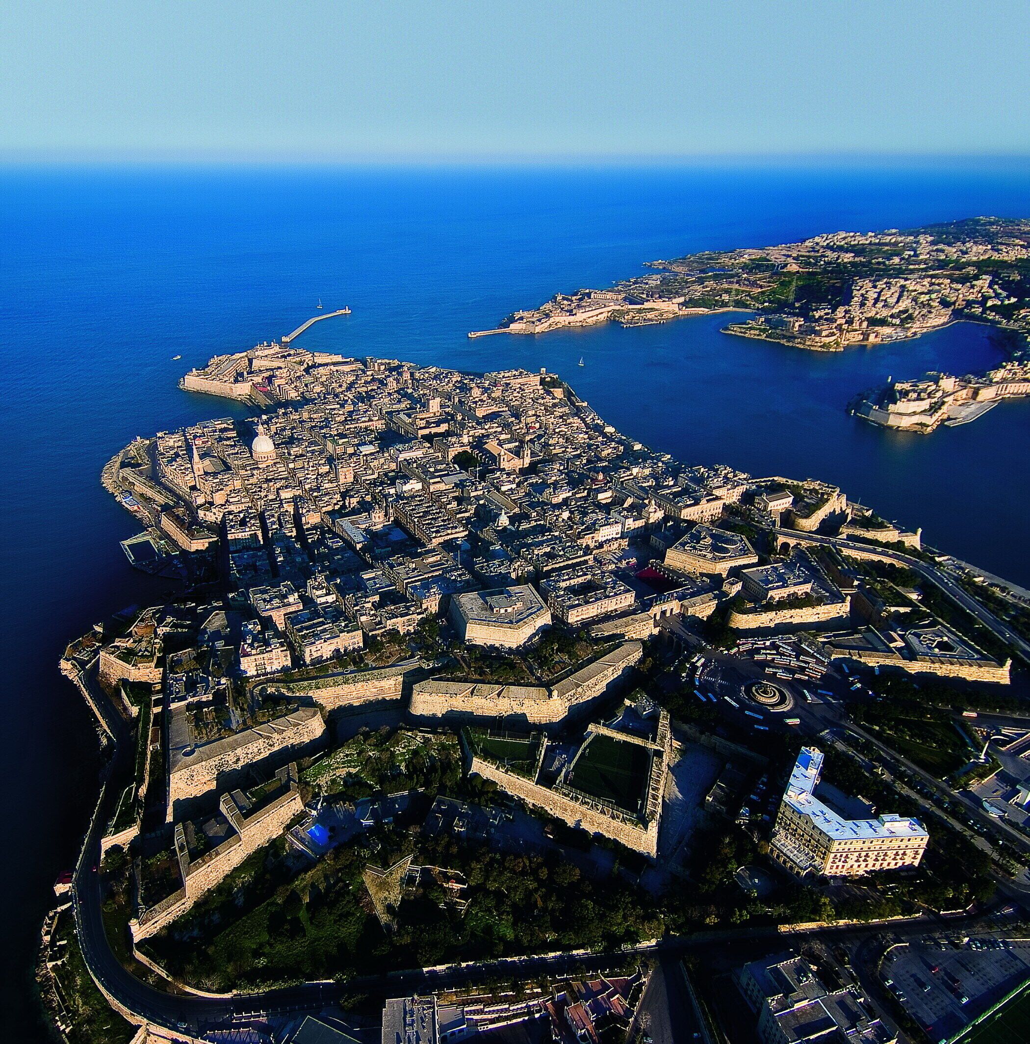An aerial view of a coastal city with a prominent fortress, a cathedral, and a mix of historical and modern buildings.
