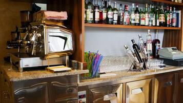 Uma área de bar com máquina de café, prateleiras de garrafas de bebidas e uma pia.