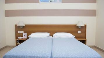 Uma cama de casal com cabeceira de madeira, duas luminárias de cabeceira, uma mesinha de cabeceira com telefone e um quadro emoldurado acima da cama.