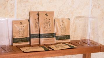 Una estantería de madera con cuatro bolsas de papel marrón etiquetadas 'Hotel Alpi' y 'Cuffia Doccia' que contienen varios artículos de aseo.