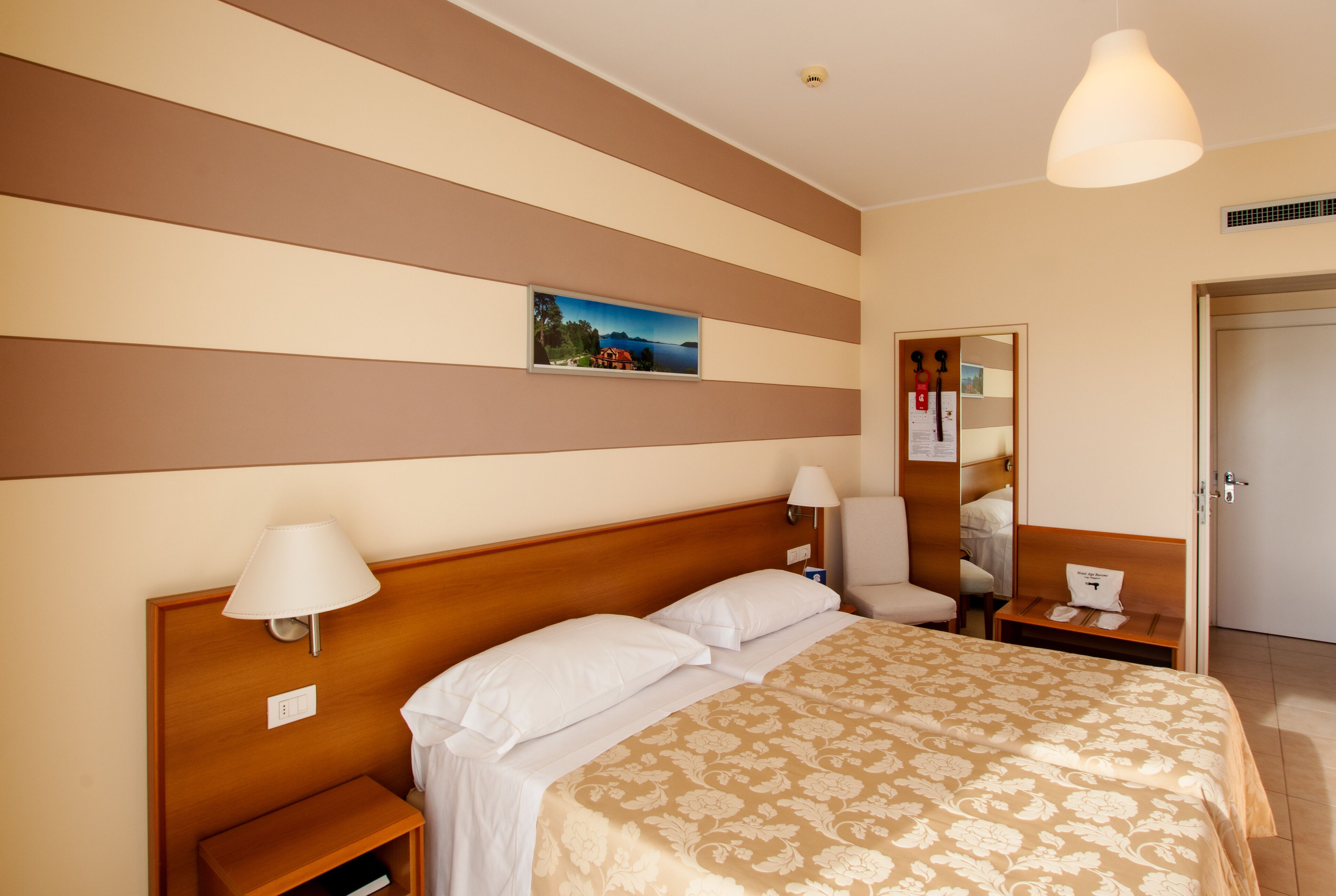 A hotel room with a large bed, a nightstand, a lamp, a mirror, and a picture on the wall.
