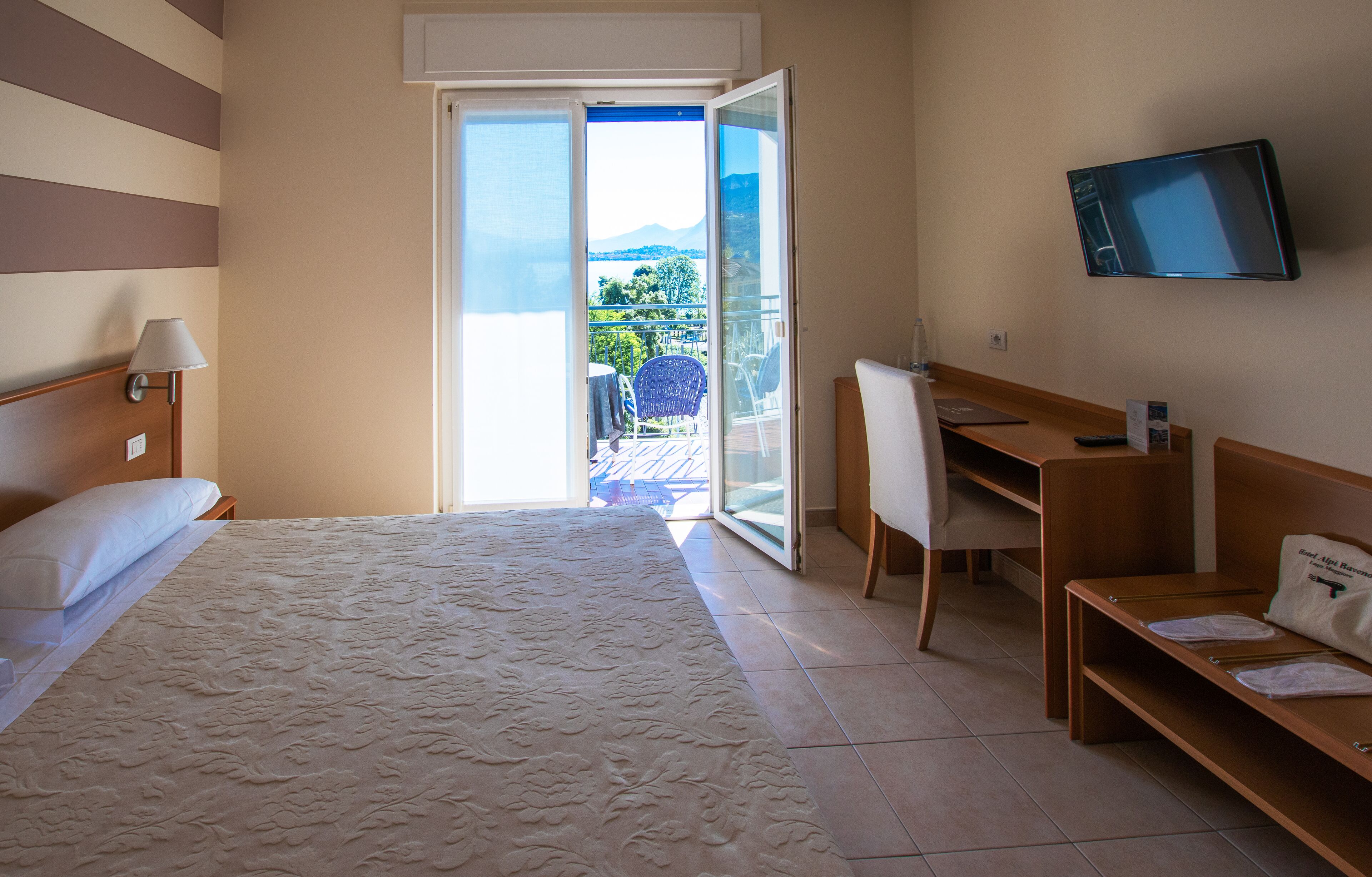 Habitación de hotel con cama, escritorio, silla, televisor y balcón con vistas.