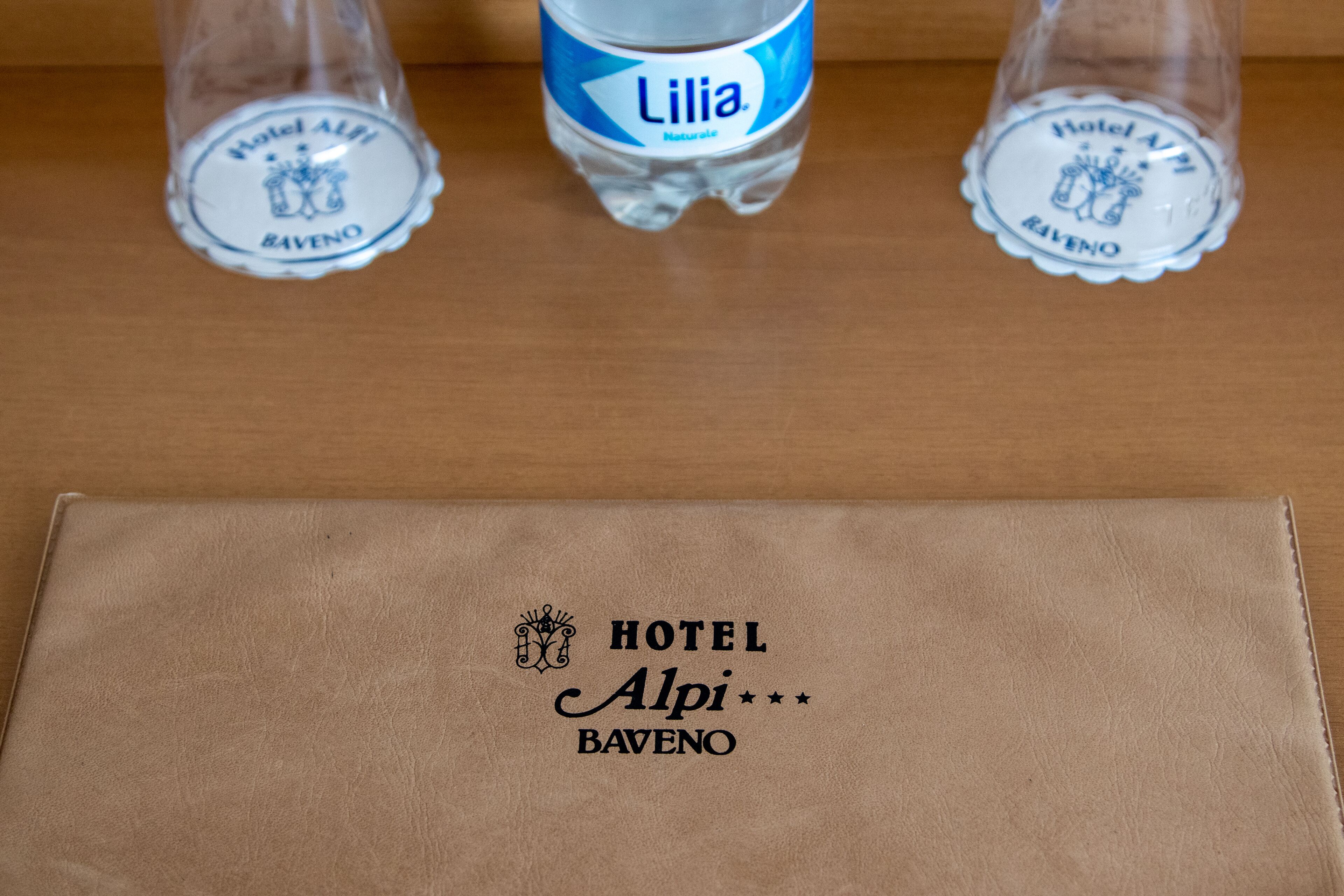 A brown leather folder with the Hotel Alpi Baveno logo and a bottle of Lilia water.