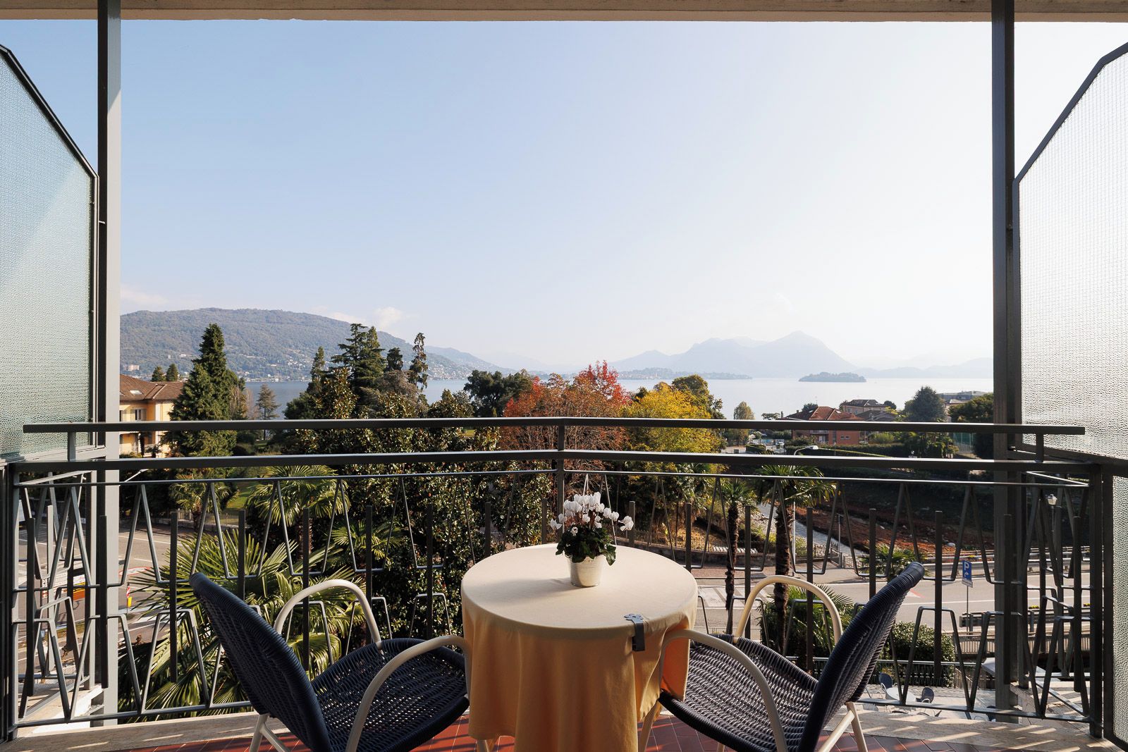 A balcony with a table and chairs, overlooking a lake and mountains.