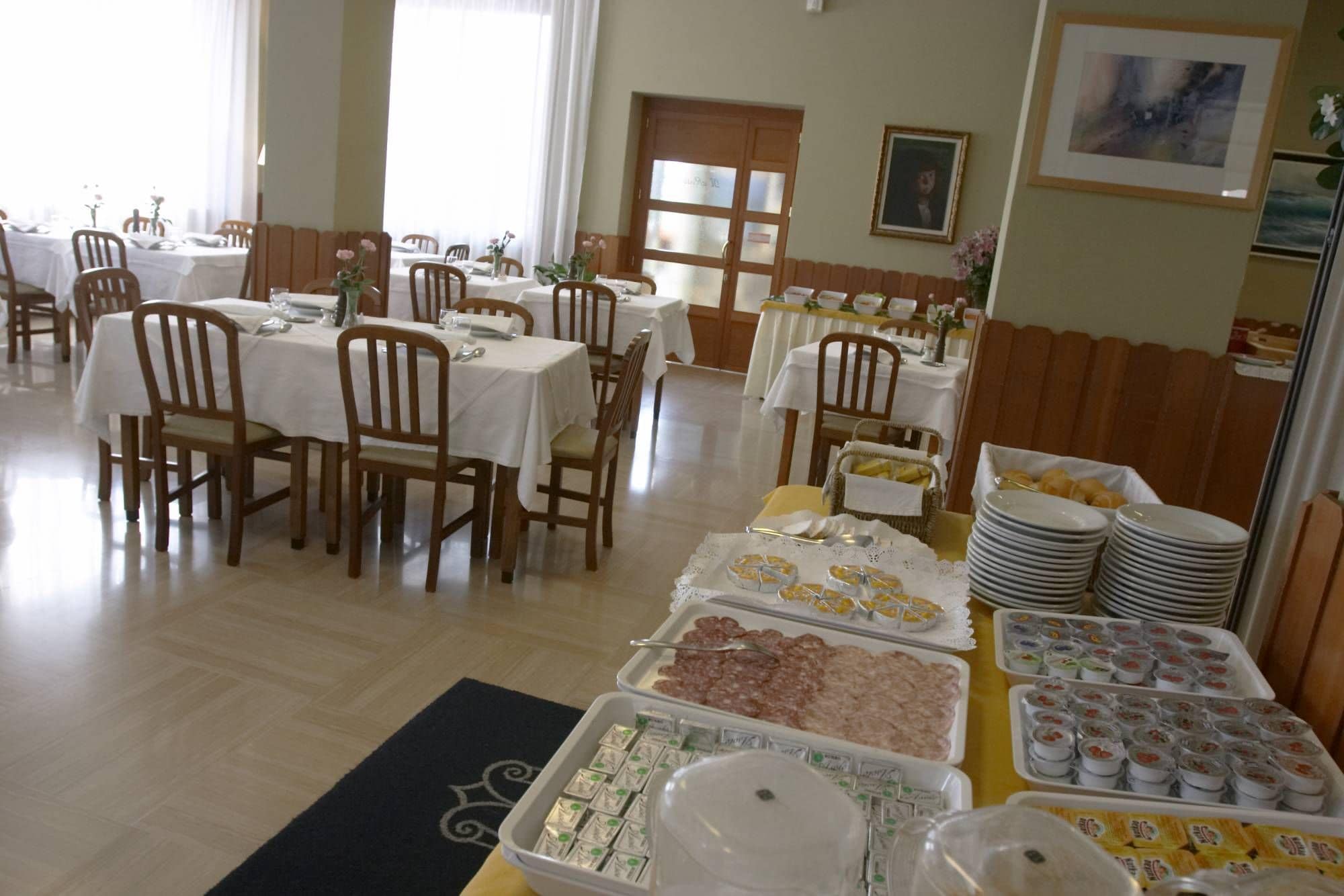 A dining area with multiple tables set for a meal, featuring a buffet with various food items and condiments.
