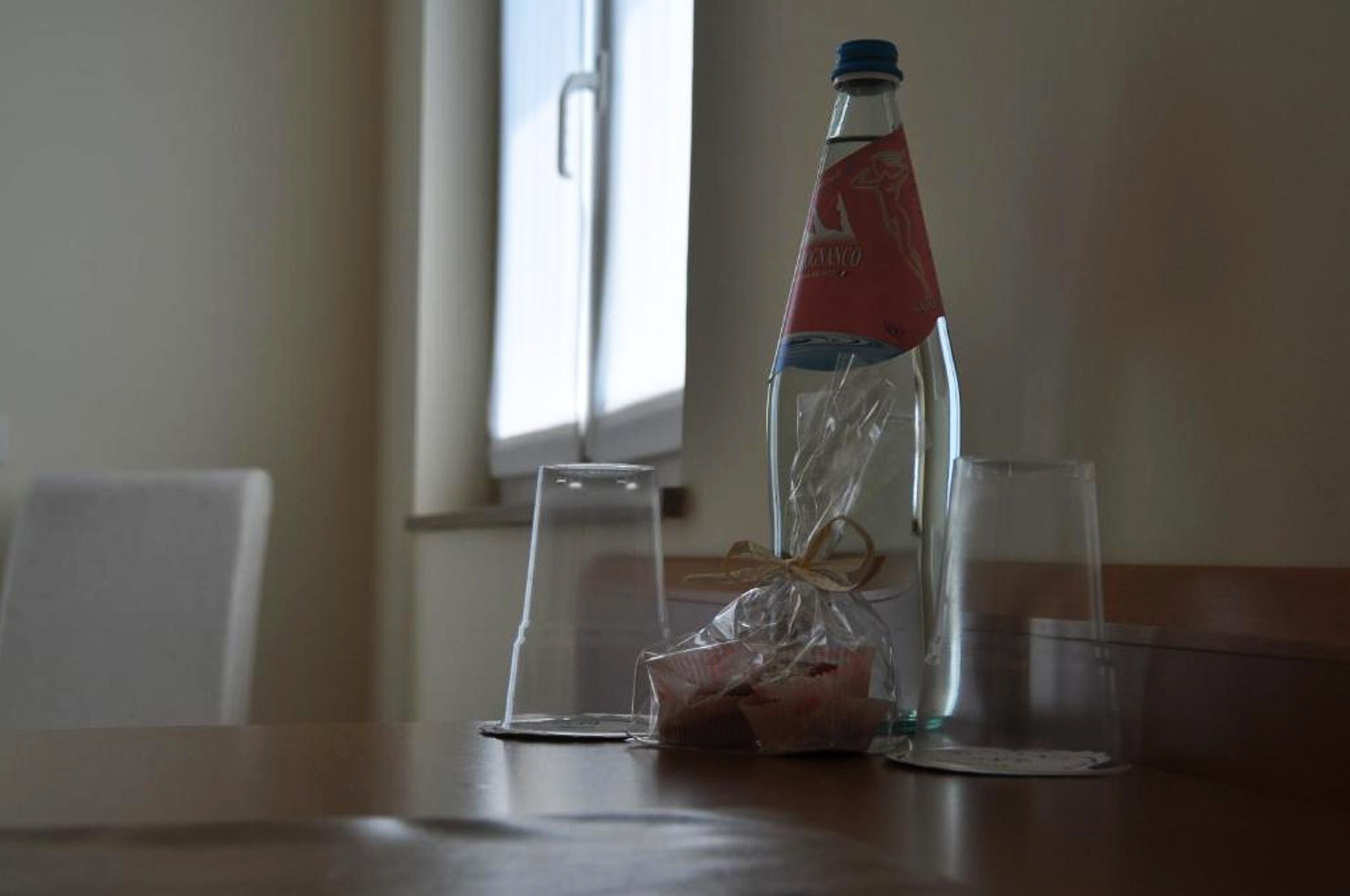 Una bottiglia d'acqua, un sacchetto di plastica e due bicchieri trasparenti su un tavolo di legno.