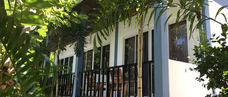 A modern building with large windows and a balcony, surrounded by lush greenery.