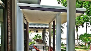 A covered outdoor area with a hammock, a chair, and a view of a garden and building in the background. - Benjamin Hut (Ko Pha-ngan)