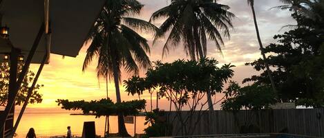 A beachside pool area with palm trees and a sunset view.