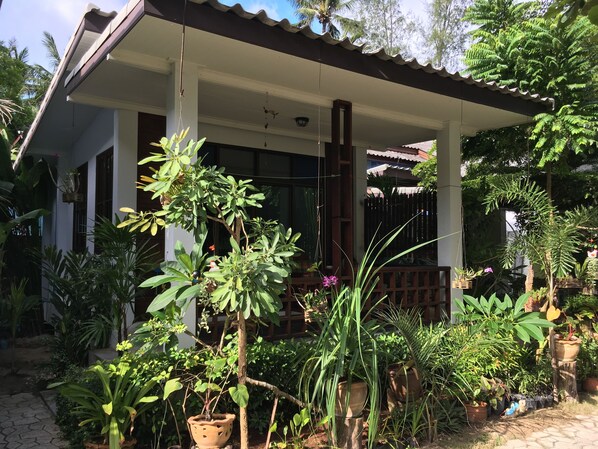 A covered porch with a white railing, surrounded by various potted plants and greenery.