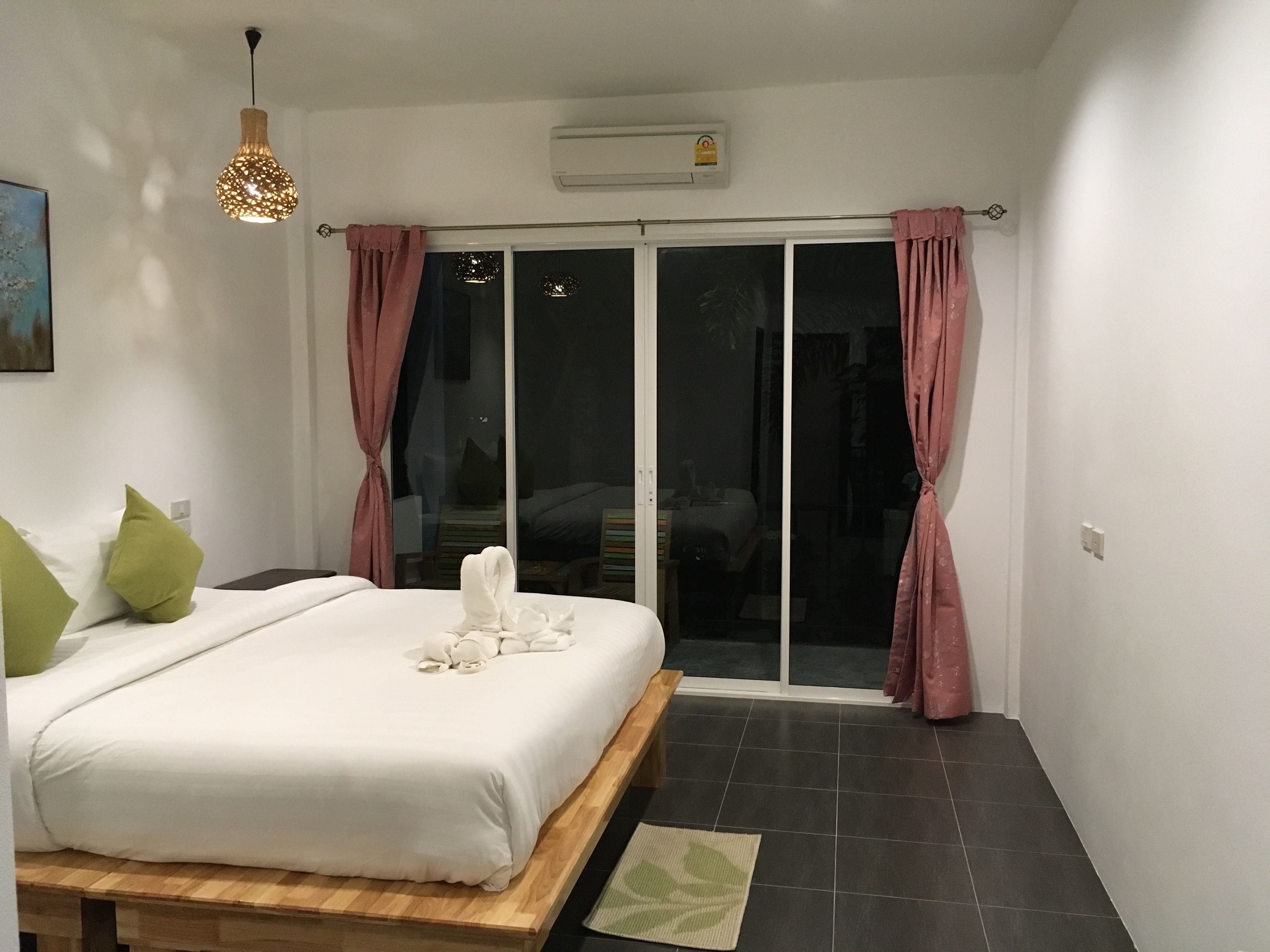 Une chambre à coucher avec un lit, un banc en bois, un tapis vert et un luminaire suspendu.