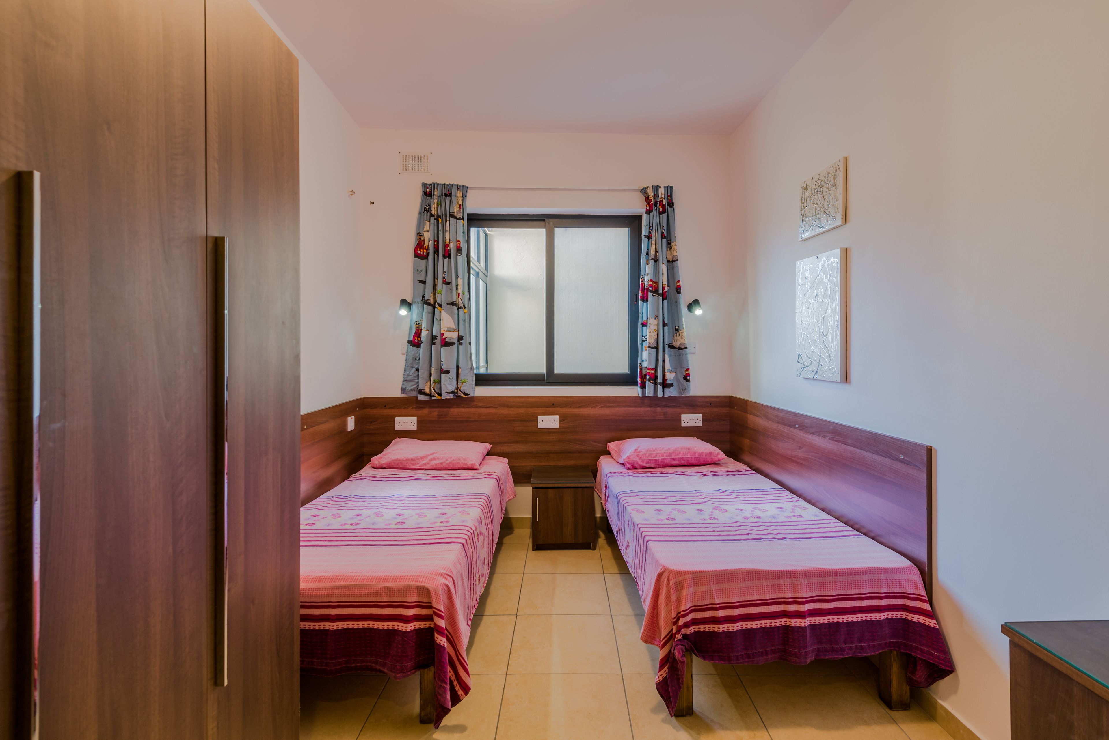 Une chambre avec deux lits, une fenêtre avec des rideaux et une armoire en bois.