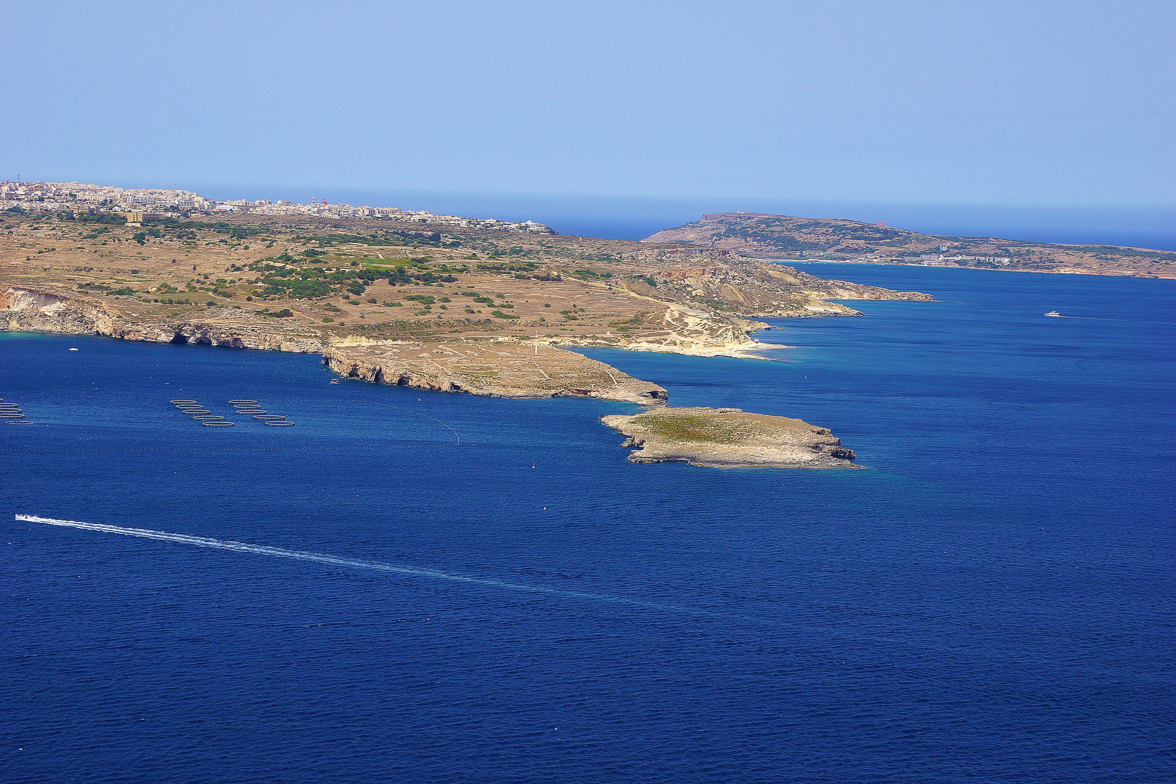 Un paysage côtier offrant une vue dégagée sur la mer, un terrain rocheux et une ville située au loin.