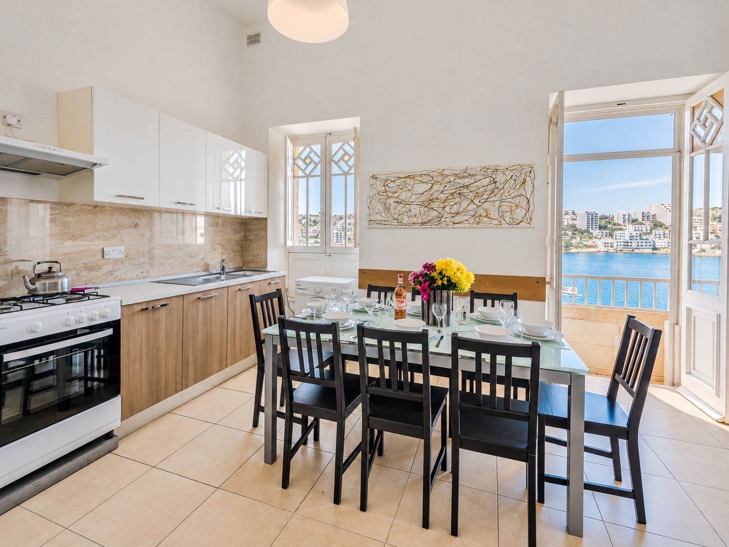 A modern kitchen with a dining area, large windows, and a view of the sea.