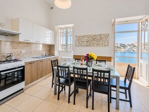 A modern kitchen with a dining area, large windows, and a view of the sea. - Blue Harbour 2 by Getaways Malta (St. Paul's Bay)