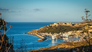 A coastal town with a marina, buildings, and a hilltop fortress. - Blue Harbour 1 by Getaways Malta (St. Paul's Bay)