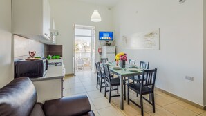 A modern kitchen with a built-in microwave, a dining area with a glass table and chairs, and a TV mounted on the wall. - Blue Harbour 1 by Getaways Malta (St. Paul's Bay)