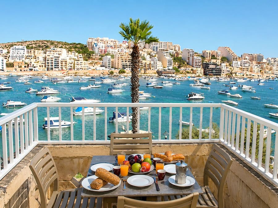 Balcón con mesa lista para el desayuno, con vista a un puerto deportivo lleno de barcos.