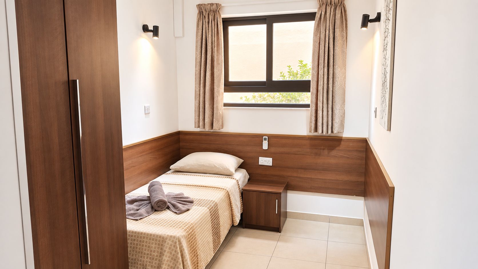 Una camera compatta con un letto singolo, comodino e finestra con tende.