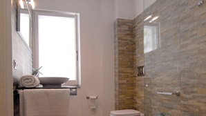 Une salle de bain moderne avec une douche à parois de verre, des toilettes et un bidet. Une fenêtre laisse entrer la lumière naturelle et une serviette est accrochée au mur.