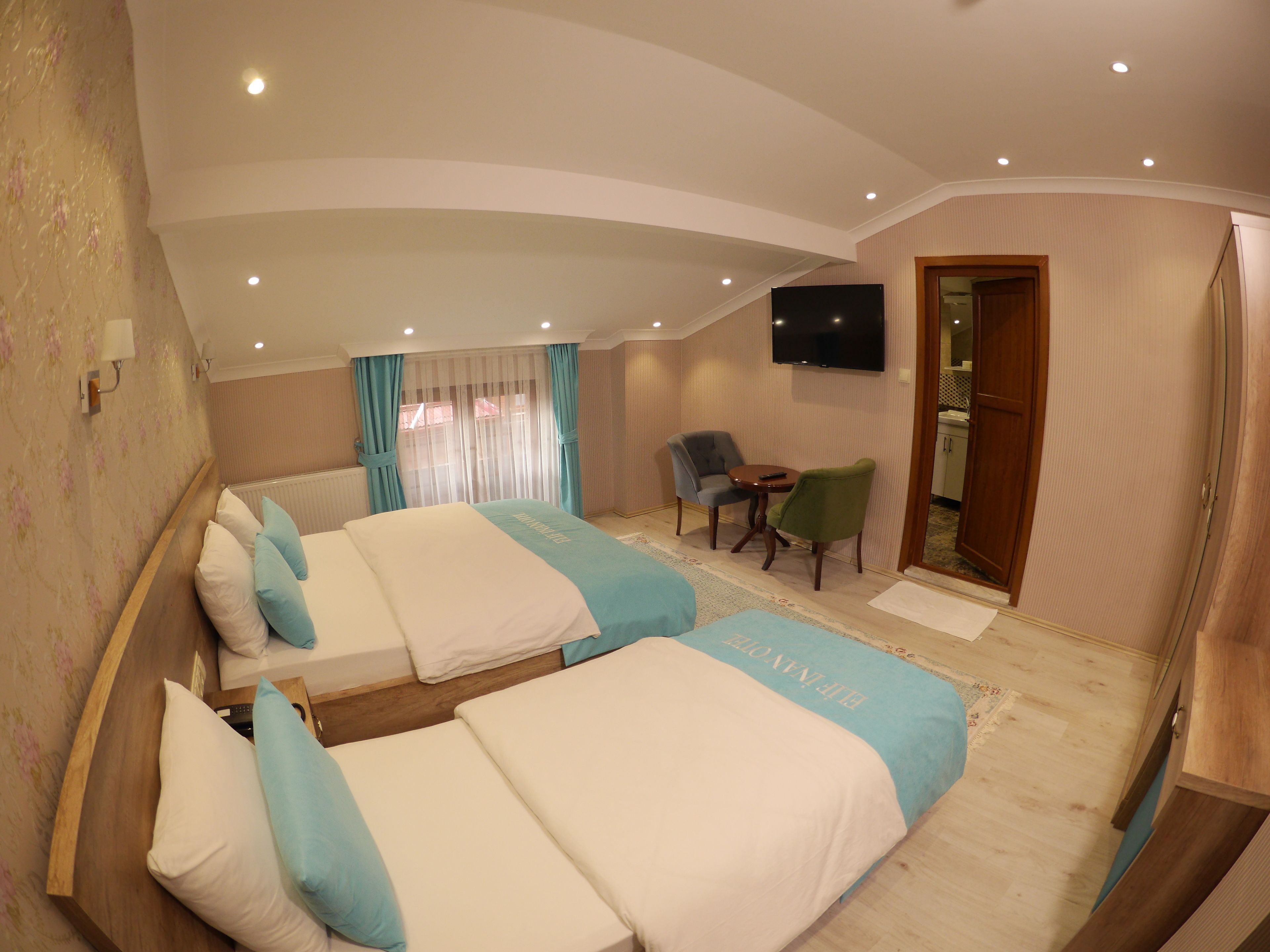 Quarto de hotel com duas camas, uma televisão, uma mesinha e uma cadeira.