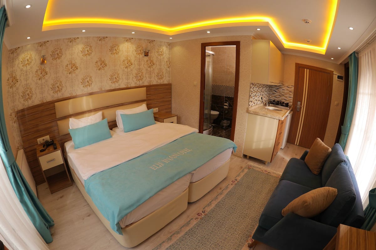 A hotel room with a bed, a sofa, a small kitchenette, and a bathroom visible through an open door.