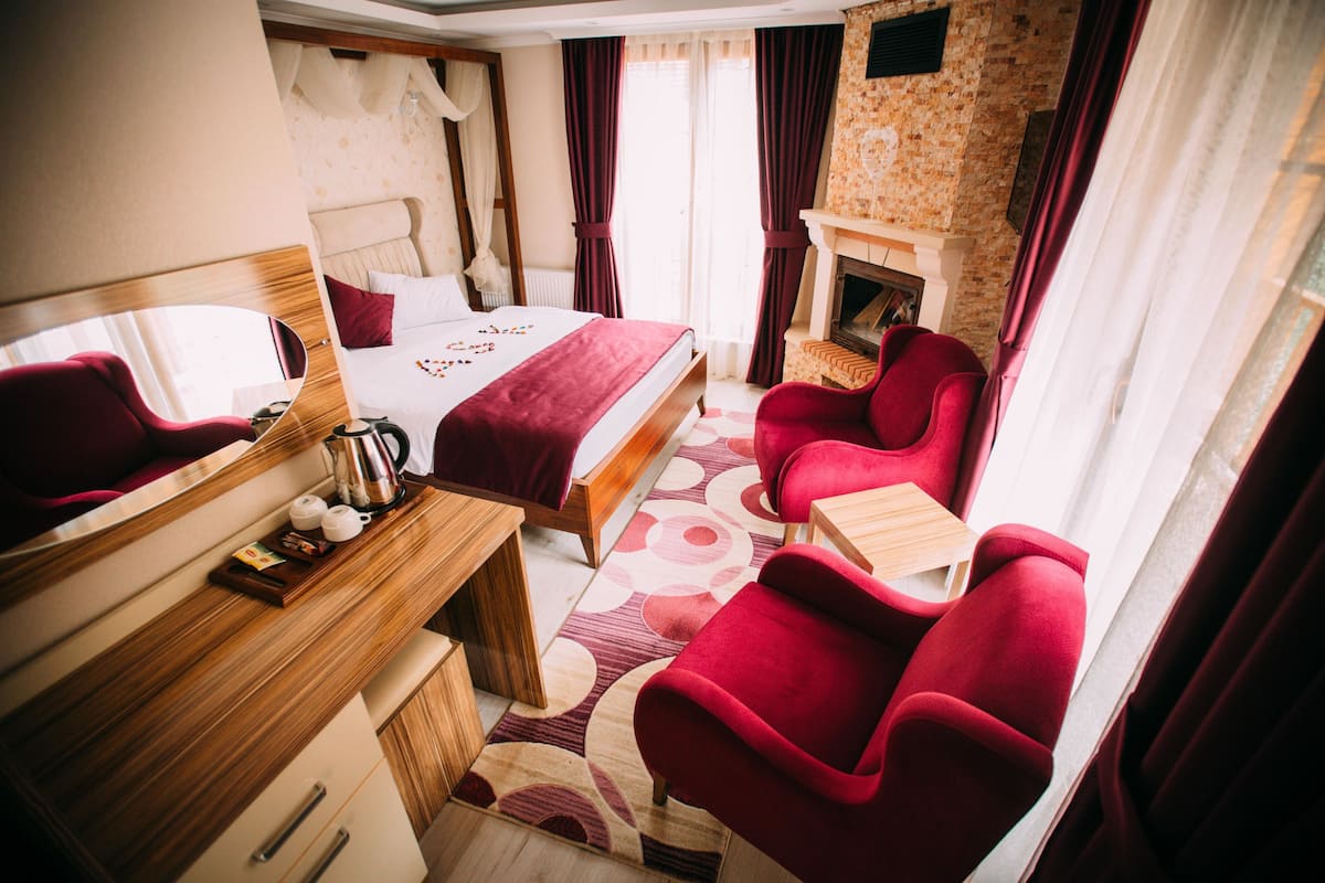 A hotel room with a bed, a desk, a chair, a fireplace, and a large mirror.