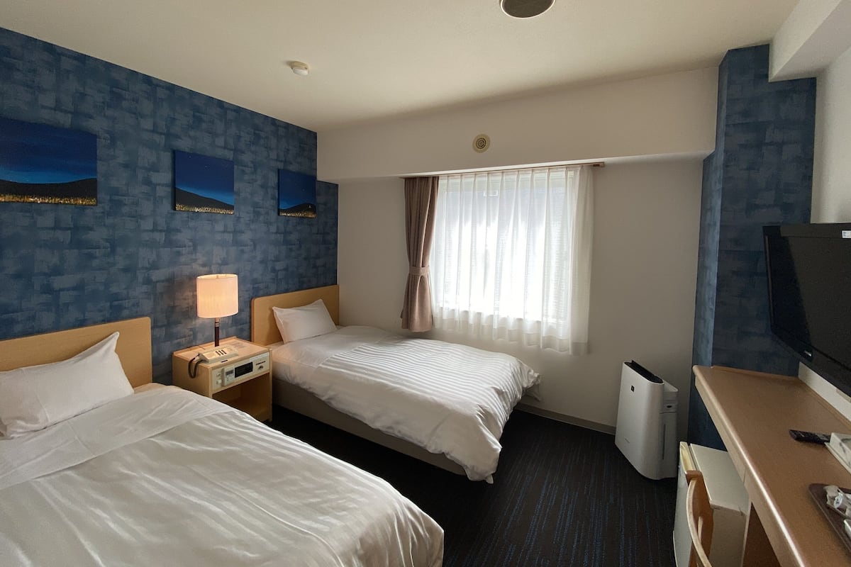 Une chambre d’hôtel avec deux lits, un bureau, une télévision et une fenêtre avec des rideaux.