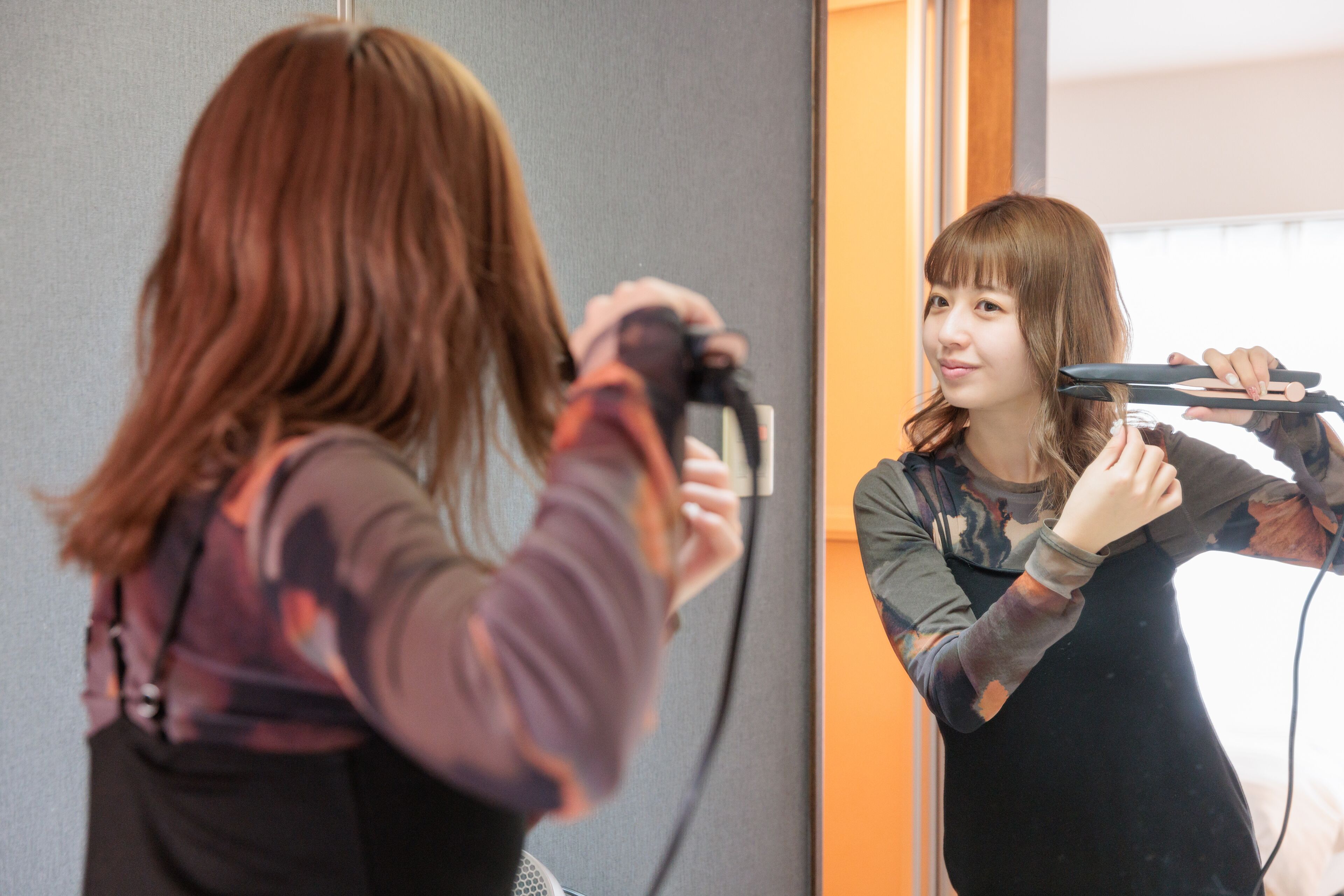 A person using a hair straightener in front of a mirror.