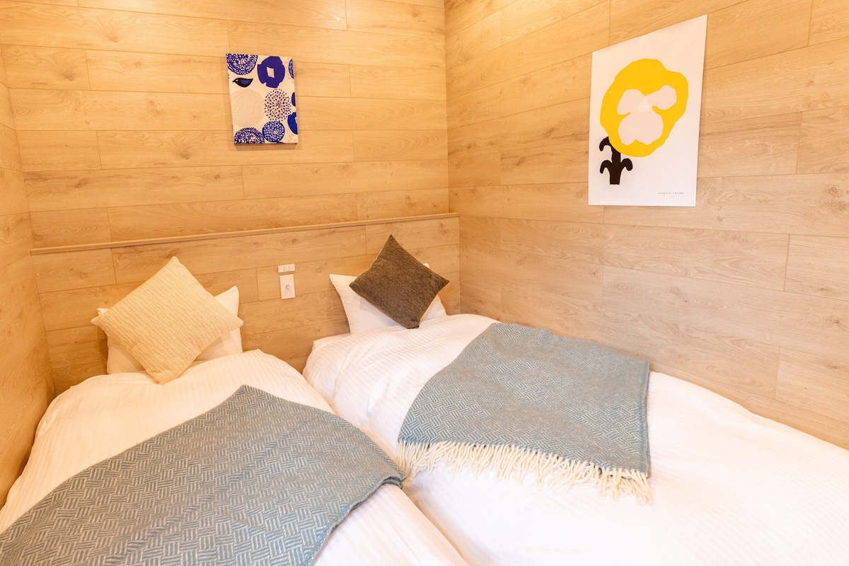 A room with wooden walls, a bed with white bedding, two pillows, a blanket, and a wall-mounted artwork.