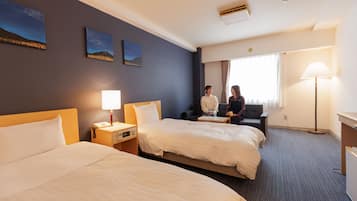 A hotel room with two beds, a nightstand with a lamp, a desk, and a chair. There are two paintings on the wall.