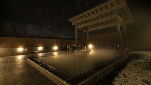 Lämmitetty ulkouima-allasalue yöllä, jossa on puinen pergola ja aurinkotuoleja.