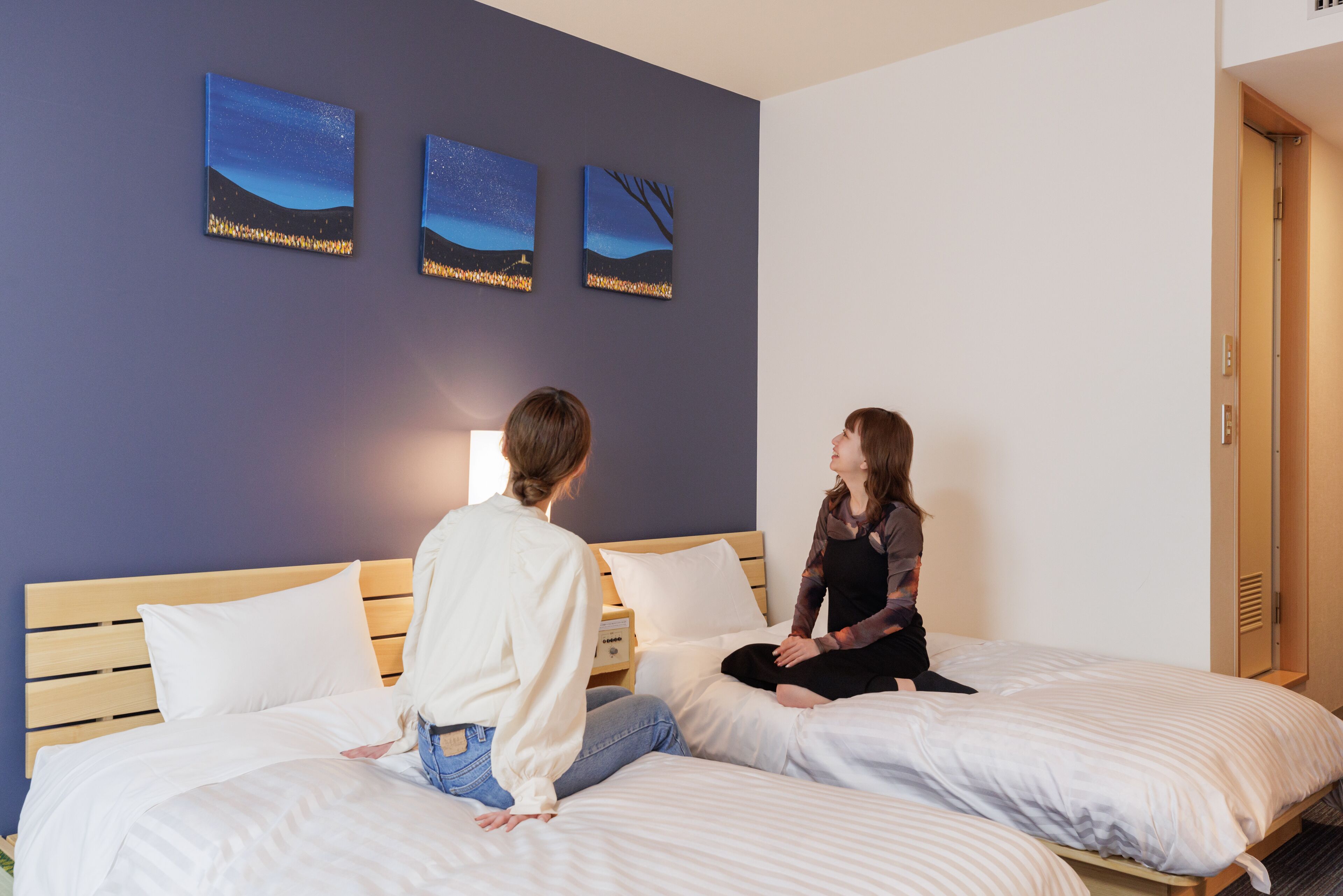 A double bed with white linens, a wooden headboard, and a nightstand with a lamp. There are three framed artworks on the wall above the bed.